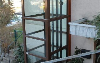 Gläserner Aufzug in Holzoptik außen