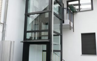 Außenaufzug aus Glas neben zweistöckigem Haus