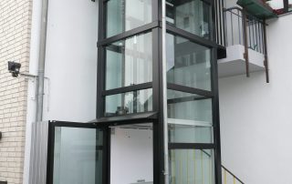Außenaufzug mit Zugang über eine Art Balkon im 1. Stock