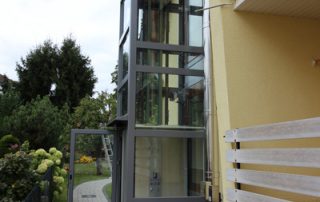 Außenaufzug aus Glas passend eingebaut neben mehrstöckigem Haus